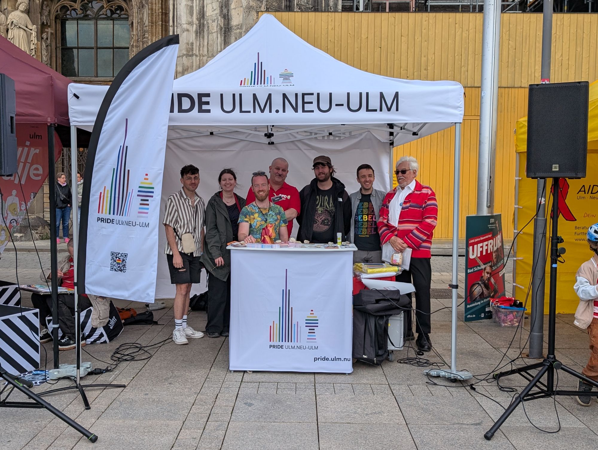 Mehrere Menschen stehen unter Pavillon von Pride Ulm und lächeln in Kamera